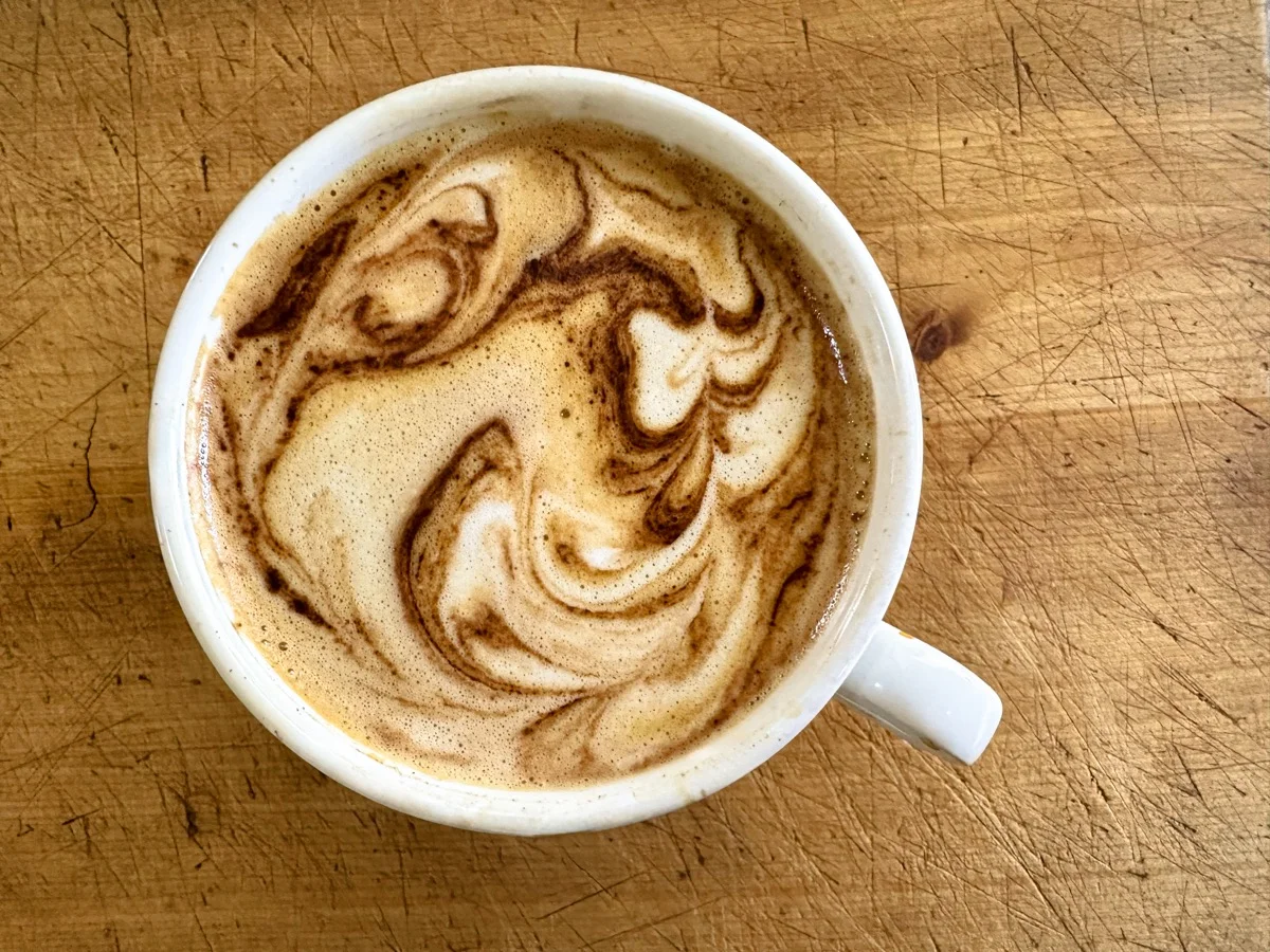 Marie Feutrier enjoying cappuccino in cozy café setting with camera